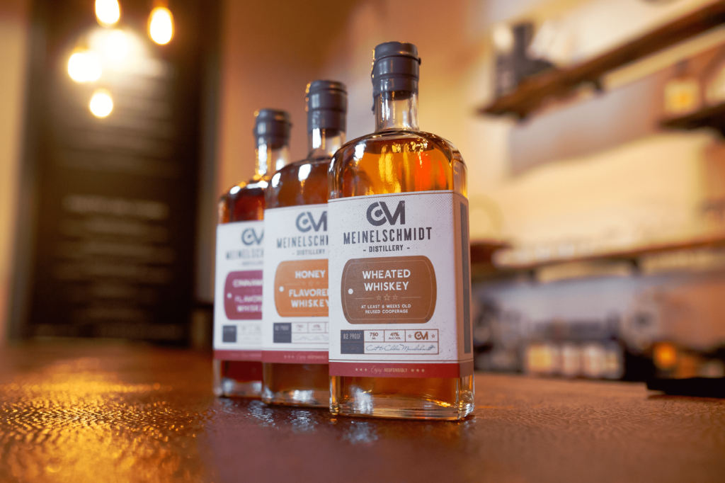 Three bottles of whiskey from Meinelschnitt Distillery are lined up on a wooden surface. The foreground bottle is labeled