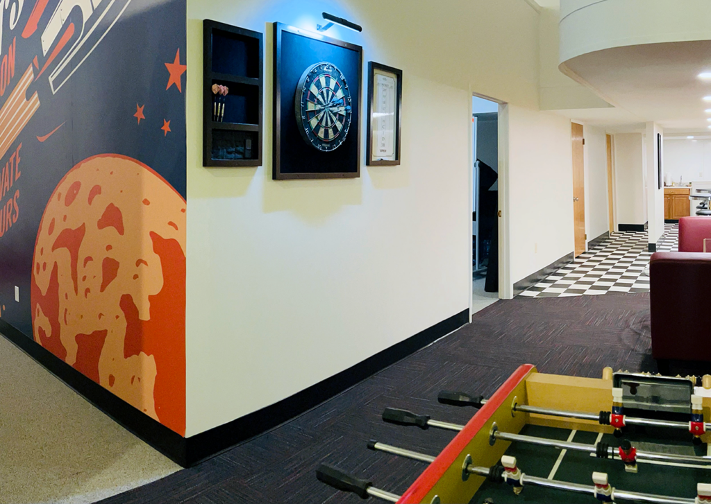 The break area of DatAchieve Digital, in which a dartboard and foosball table are visible.