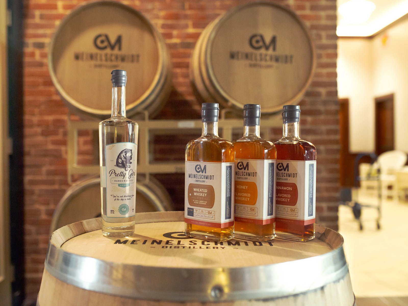 Bottles of different spirits are displayed on a barrel, with large barrels labeled